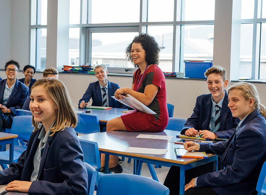 A teacher and students in a classroom all smiling.